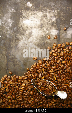 Zerstreuten Haufen von aromatischen frisch gerösteten Kaffeebohnen mit einer kleinen Metall-Kugel auf einem Grunge Hintergrund mit Exemplar Stockfoto