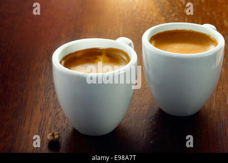 Zwei Espresso Kaffee in kleinen weißen Tassen, mit einer einzigen Kaffeebohne ruht auf dem Holz Hintergrund Stockfoto