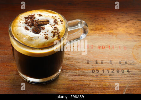 Schaumigen Tasse Espresso Kaffee oder Cappuccino, garniert mit Schokolade bestreut und einer einzigen Kaffeebohne auf eine alte hölzerne Oberfläche mit Zahlen versehen Stockfoto