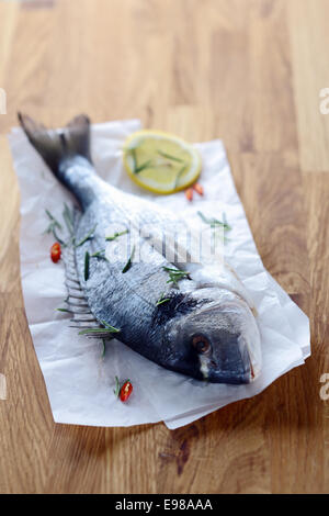 Ganze rohe Fische auf zerknittertes Papier liegen auf einem Holz Küchentisch warten darauf, gerundet werden, um eine angenehme Seafood-Dinner zubereiten Stockfoto