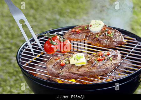 Zartes Steak mit einer Locke von Butter und Kräutern Grillen im Freien auf einem tragbaren Grill mit einer zinkige Gabel und Tomaten garniert Stockfoto