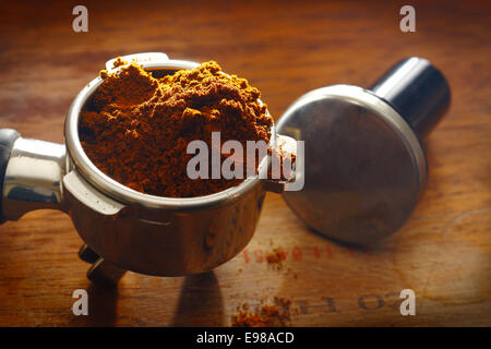 Frisch gemahlener Kaffee überlaufen über den Rand des einen Metallfilter auf einer Holzfläche mit Messlöffel Stockfoto