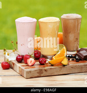 Drei Gläser leckere verschiedene natürliche Protein Cocktails umgeben von frischem Obst: Kirschen, Zitrone und Erdbeeren Stockfoto