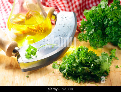 Nahaufnahme von einem modernen Kraut Cutter (Wiegemes) mit Holzgriffen und ein Bund Petersilie auf der Klinge. Stockfoto