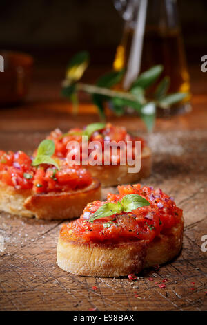 Bunte rote Tomate Bruschetta auf Scheiben von Crisp knusprig geröstet oder gegrilltes Baguette liegen auf einem alten Grunge schlecht erzielte Schneidbrett aus Holz, niedrigen Winkel Ansicht mit Exemplar Stockfoto