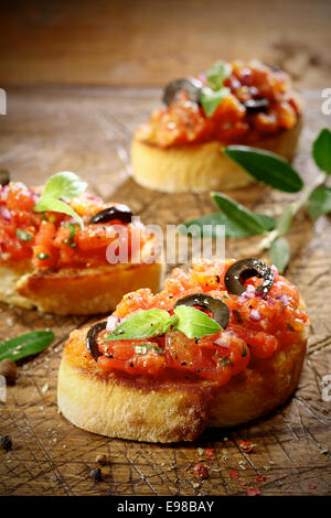 Tomaten-Bruschetta mit Olivenöl und Basilikum auf Scheiben von Crisp knusprig getoastet gekrönt oder gegrilltes Baguette liegen auf einem alten Grunge schlecht erzielte Schneidbrett aus Holz, niedrigen Winkel Ansicht mit flachen dof Stockfoto