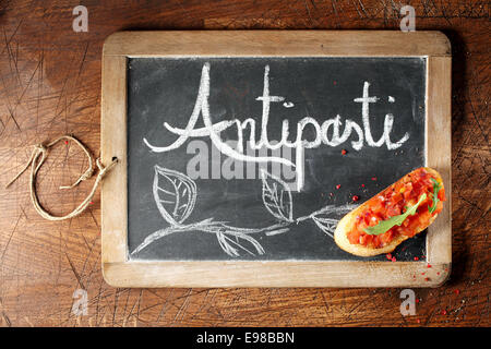 Draufsicht der bunten roten Tomaten Bruschetta auf ein Antispasti melden Sie handschriftlich auf einer kleinen gerahmten Tafel liegen auf einem hölzernen Hintergrund Stockfoto