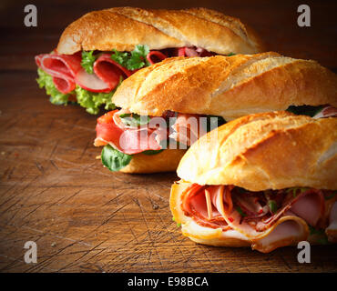 Verschiedene leckere Baguette Brötchen gefüllt mit dünn geschnittenen Schinken oder Salami und frischem grünen Salat oder Basilikum in eine schräge Reihe auf einem alten Holztisch mit Exemplar angeordnet Stockfoto