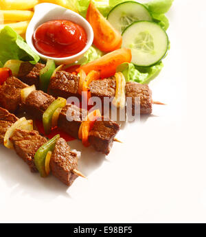 Erhöhte Ansicht von drei gegrilltes Rindfleisch und Paprika Kebab serviert mit einer Schüssel mit Tomaten-Ketchup, Pommes Frites und frischem Salat Stockfoto