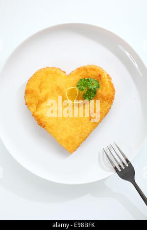 Draufsicht auf eine knusprige golden herzförmige Kalbsschnitzel Kalb Pfanne gebraten in Paniermehl mit frischer Petersilie garniert und serviert Stockfoto