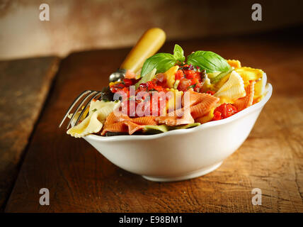 Leckere bunte italienische Farfalle serviert mit Tomaten und Basilikum in eine weiße Keramik Schüssel mit einer Gabel auf einem alten Holztisch, schräge Ansicht Stockfoto