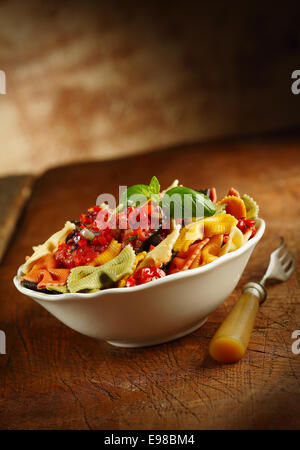 Leckere bunte italienische Farfalle serviert in einer Schüssel auf einem Holztisch in einer Landhausküche mit einer alten Gabel und Exemplar, geneigten Winkel Stockfoto