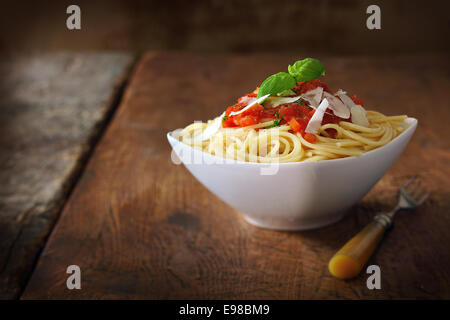 Moderne schlichte weiße Keramik Teller gefüllt mit italienischen Spaghetti mit Tomatensauce belegt und garniert mit frischem Basilikum auf einem alten Holztisch Stockfoto