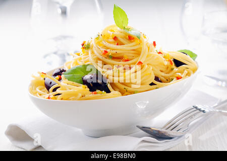 Schuss von Spaghetti Nudeln in eine Schüssel mit Oliven auf eine weiße Serviette weiß mit Weingläsern im Hintergrund hautnah. Stockfoto