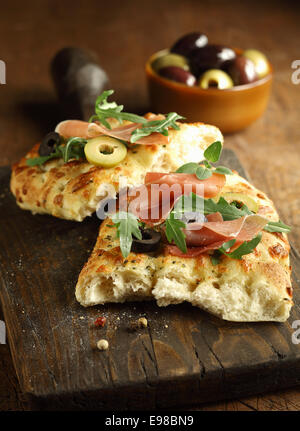 Köstliche traditionelle überbackene italienische Focaccia-Brot mit Schinken, Rucola und Oliven auf alten gekrönt geknackt Schneidbrett aus Holz Stockfoto