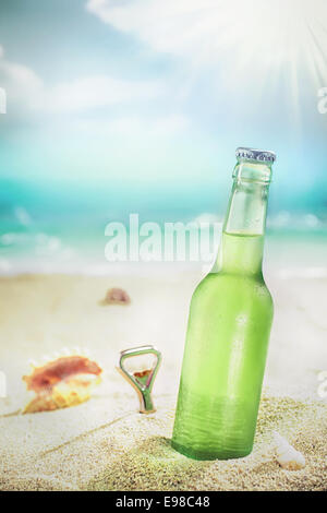 Eis-kalte grüne ungekennzeichnete Flasche erfrischendes Lagerbier oder Soda stehend im goldenen Sand an einem tropischen Strand unter den heißen Strahlen der Sommersonne Stockfoto