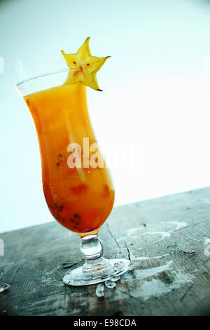 Exotische bunte orange Karambolen cocktail mit Früchten und Eis serviert in einem langen Glas auf einem alten hölzernen Theke mit verschütten Stockfoto