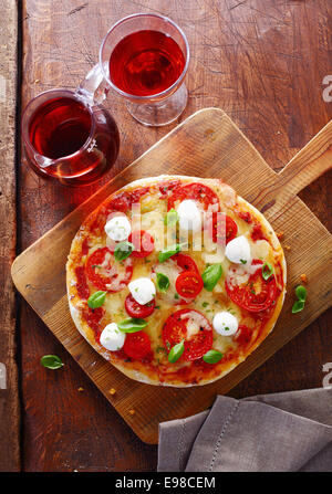 Draufsicht auf eine bunte Tricolore italienische Pizza mit Käse, Tomaten und frischem Basilikum auf einem Holzbrett serviert mit einem Krug und Glas Rotwein auf einem alten Holztisch Grunge. Mehr Pizza an meinem Anschluss. Stockfoto