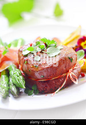 Saftige zarte Filet Steak Medaillon mit Schnur gebunden und serviert mit frischen grünen Spargelspitzen, eingehüllt in feine Scheiben geschnittenen Schinken oder Speck Stockfoto