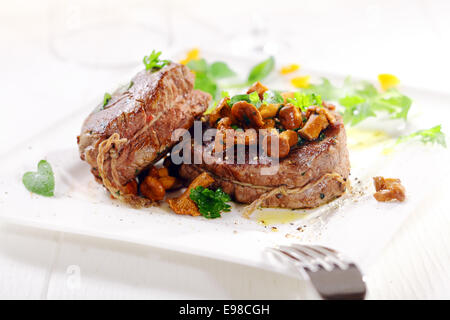 Gourmet-Abendessen der Dicke saftige Medaillons vom Filet mit Schnur garniert mit Waldpilzen gebunden und auf einem weißen Teller garniert mit Kräutern serviert Stockfoto