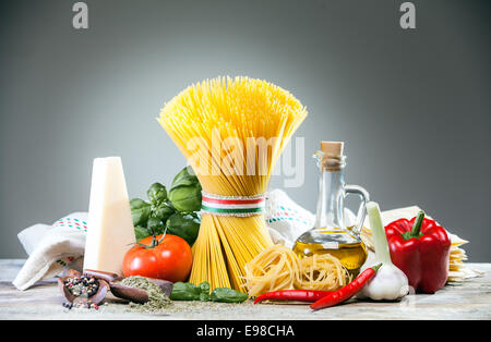 Getrocknete italienische Spaghetti, verbunden mit einem Band in den Farben der Nationalflagge - rot, weiß und grün, auf einer Theke mit Käse, Tomaten, Basilikum, Chili-Pfeffer, Knoblauch, Olivenöl und Paprika auf grau Stockfoto