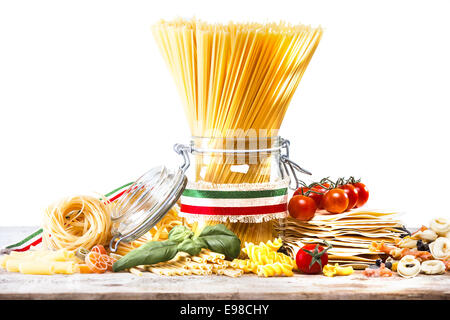 Verschiedene getrocknete italienische Teigwaren wie Spaghetti mit einem Band in den Farben der Nationalflagge, Cherry-Tomaten, Fettucini gebunden, getrockneten Lasagne Pasta und Basilikum auf einer Küchenarbeitsplatte Stockfoto