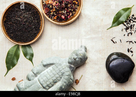 Kräuter-Tee-Blätter für alternative Therapie in zwei kleine Schüsseln mit einem asiatischen Statue und Spa massage Steinen auf einem leicht strukturiertem Textil-Hintergrund Stockfoto