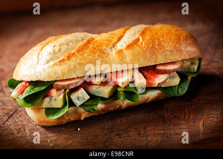 Knusprig goldene Baguette mit einer herzhaften Füllung aus geschnittenen Feigen, Blauschimmelkäse und frischem Spinat Blätter auf einem rustikalen Holztisch Top mit Eckansicht Vignettierung, hoher Winkel Stockfoto