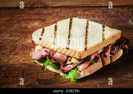 Gegrilltes Sandwich von einem Grill mit seltenen Roastbeef und frischen grünen grünen Kräutern auf einem rustikalen Holztisch Stockfoto