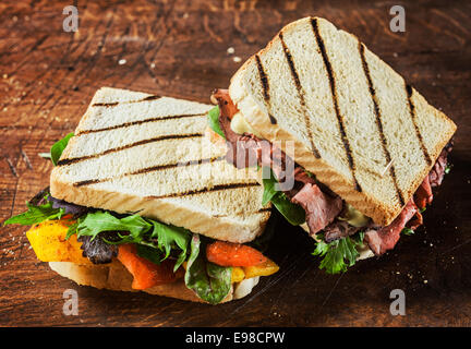 Leckere gegrillte Sandwiches aus einem Sommer BBQ gefüllt mit Roastbeef, Kräuter und eine Auswahl an frischen Salatzutaten auf einem rustikalen Holztisch angezeigt Stockfoto