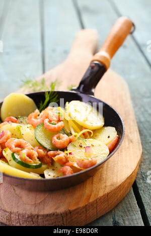 Garnelen, Zucchini und Kartoffel Pfanne gebraten und serviert in der Pfanne auf einem Holzbrett für einen gesunden, frischen Fisch essen Stockfoto