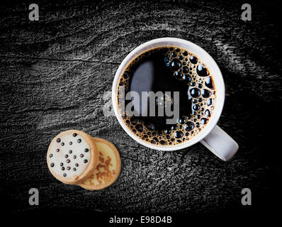 Draufsicht auf eine Tasse frisch gebrühten heißen Espressokaffee serviert auf einem verwitterten Grunge rustikalen Holztisch mit zwei vereisten Kekse Stockfoto