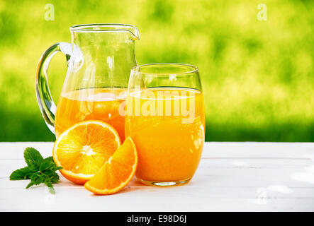 Eine Kanne und ein Glas frisch gepresster Orangensaft, garniert mit einem Zweig Minze, Orange, im Freien im Sommer. Stockfoto