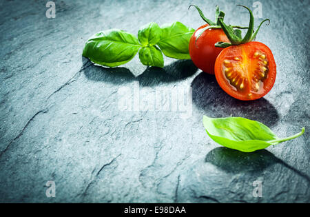 Frischem Basilikum und Traube Tomaten Grenze in der oberen rechten Ecke des Rahmens auf einen strukturierten rissige Hintergrund mit Exemplar angeordnet Stockfoto