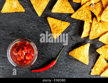 Knusprig goldene Mais Totillas mit scharfer Salsa-Sauce und ein hot Chili Paprika für einen würzigen Snack, Draufsicht auf eine Schieferoberfläche Stockfoto