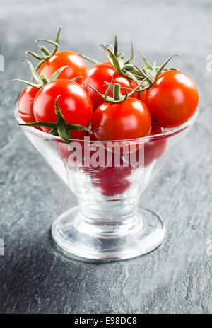 Frische reife rote saftige Cherry Tomaten mit Stielen serviert in einem konischen Glasbehälter als Crudites, Tauchen Sie ein in eine pikante sauce Stockfoto