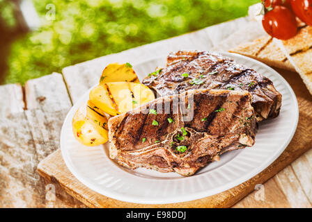 Portion Gegrillte Lammkoteletts garniert mit gehackten frischen Kräutern und Kartoffeln bei einem Barbecue auf einem rustikalen hölzernen Picknick-Tisch im Garten Stockfoto