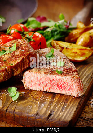 Portion gesunden mageres gegrilltes Rindfleischsteak geschnitten durch offenbaren das seltene Interieur serviert auf einem Holzbrett mit gebratenem Gemüse Stockfoto