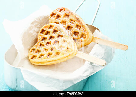 Zwei herzförmige Waffeln am Stiel in einer Blechdose eine ein Papier wickeln, mit Zucker und Zimt bestreut Stockfoto