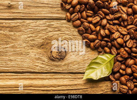 Haufen von frisch gerösteten Kaffeebohnen angeordnet als Ecke Grenze auf strukturierte rustikalen Holzbretter mit Rohkaffee Blatt und Exemplar Stockfoto