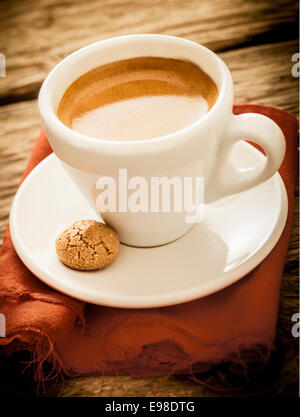 Portion heiße aromatischen Espressokaffee in eine schlichte weiße Tasse mit Makronen auf einem rustikalen Tuch und alte Grunge strukturierte Holztisch serviert Stockfoto