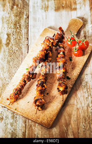 Trio von würzig gegrillte Spieße und Braten Tomaten serviert auf ein Schneidbrett aus Holz an einem Sommer-Grill, erhöhte Ansicht auf einem alten Stockfoto