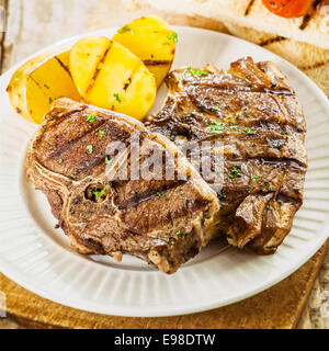 Nahaufnahme einer Portion zwei saftig gegrillte Gegrillte Lammkoteletts gewürzt mit frischen Kräutern, serviert mit Kartoffeln bei einem Sommerpicknick Stockfoto