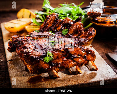 Köstlichen gegrillte Rippchen mit pikanter Heften Sauce gewürzt und serviert mit gehackten frischen Kräutern auf eine alte rustikale Schneidbrett aus Holz in einer Landhausküche Stockfoto