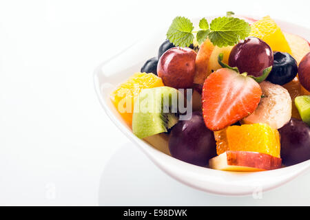 Appetitlich Schüssel mit frischem Obstsalat mit Erdbeeren, Heidelbeeren, Trauben, Banane, Kiwi, Apfel und Orange, gekrönt mit einem Zweig frische grüne Pfefferminze, Closeup weiß mit Exemplar Stockfoto