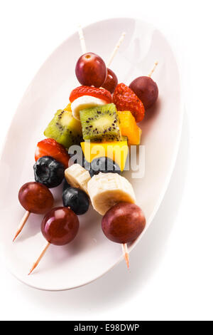 Serving of colorful healthy tropical fruit kebabs on wooden skewers with grapes, banana, orange, kiwifruit and strawberry on an Stockfoto