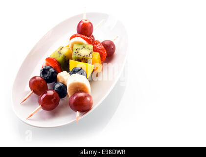 Frische gesunde tropische Früchte Spieße mit Trauben, Heidelbeeren, Bananen, Orangen, Kiwis und Erdbeeren serviert auf einem weißen oval Stockfoto