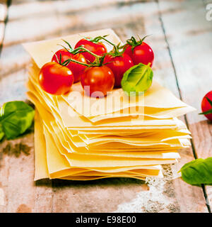 Getrocknete ungekochte Teigwaren Lasagneblätter mit frischen Zutaten wie Cherry-Tomaten und Basilikum-Blätter, hautnah alte Holzbretter Stockfoto