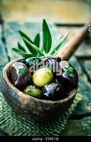 Alte hölzerne Schöpfkelle oder großen Löffel gefüllt mit erfahrenen schwarze und grüne Oliven, dekoriert mit einem Olivenbaum Zweig Stockfoto