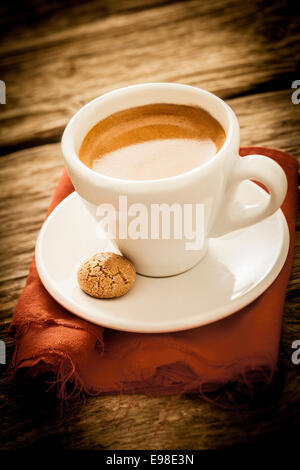 Frisch gebrühter Espressokaffee in einer Landhausküche serviert in eine schlichte weiße Tasse und Untertasse mit einer leckeren Makronen für ein erfrischendes Getränk von morgen, mit Exemplar und Vignettierung Stockfoto